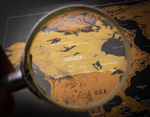 Hand holding magnifying glass and focus to CANADA map