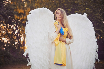girl dressed as an angel in the evening garden with Ukrainian flag