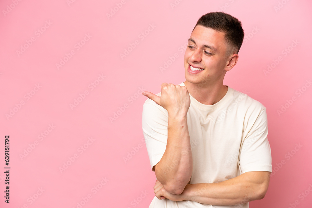 Wall mural Young Brazilian man isolated on pink background pointing to the side to present a product