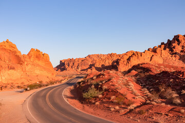 Panoramic sunrise view of endless winding empty road in Valley of Fire State Park leading to red Aztec Sandstone Rock formations and desert vegetation in Mojave desert, Overton, Nevada, USA. Freedom