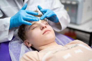 Naklejka premium a cosmetologist doctor makes cosmetic procedures on the face of a young guy in a beauty salon