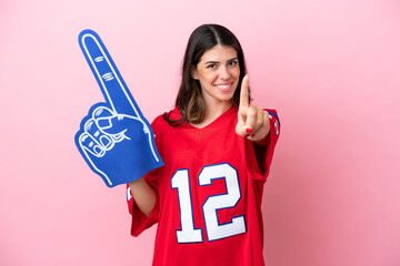 Young Italian fan woman with foam hand isolated on pink background showing and lifting a finger