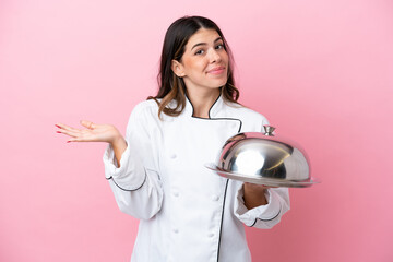 Young Italian chef woman holding tray with lid isolated on pink background having doubts while...