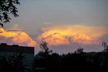 Fluffy clouds with colored tints. Clouds in the form of cotton wool. Large accumulations of clouds after rain. Clouds illuminated by the sun at sunset.