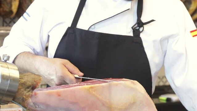 Professional ham cutter working with knife and barehand at butcher shop cutting thin slices of Iberian ham