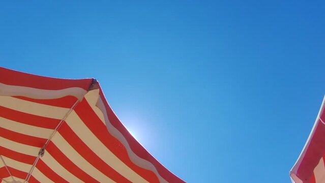 Summer time. Orange striped parasol under beautiful blue sky on background.