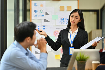 Asian female employee standing in front of flip chart giving presentation at meeting