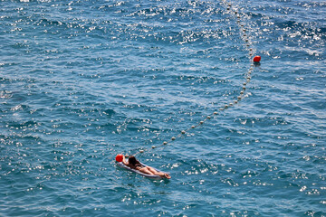 Młoda dziewczyna w stringach płynie na materacu po morzu.  - obrazy, fototapety, plakaty