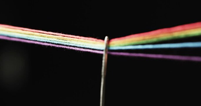 Video of micro of rainbow coloured threads going through needle with copy space on black background