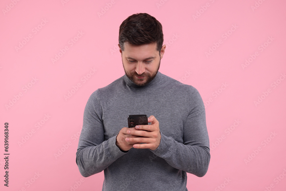 Wall mural Happy man using smartphone on pink background