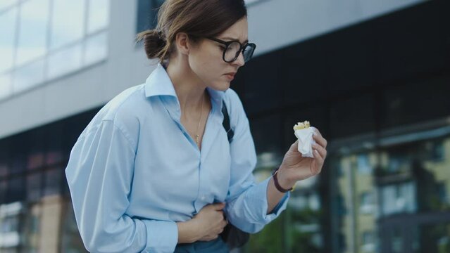 Woman eating unhealthy snack but feeling stomach pain and cramps, diarrhea