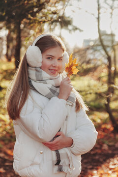 Portrait of perfect teen cover girl with fall leaves in autumn park, smiling looking at camera. Cute young lady model in white jacket in autumn forest. Leisure activity concept. Copy ad text space