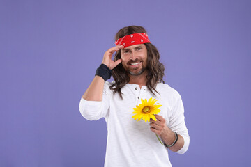 Stylish hippie man with sunflower on violet background