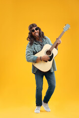 Fototapeta na wymiar Stylish hippie man playing guitar on orange background