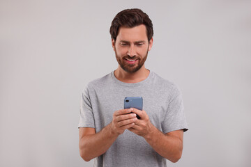Handsome bearded man using smartphone on grey background