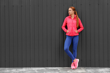 Beautiful woman in gym clothes near dark grey wall on street, space for text