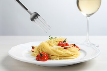 Eating tasty capellini with tomatoes and cheese at white wooden table, closeup. Exquisite presentation of pasta dish