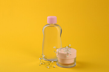 Bottle with baby oil, cream and gypsophila on yellow background