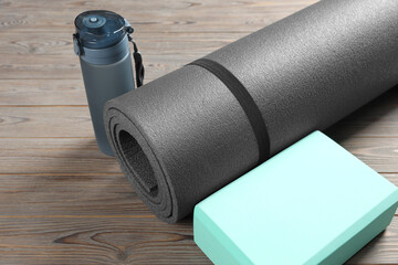 Exercise mat, yoga block and bottle of water on wooden floor