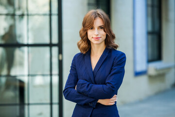 Portrait of a beautiful young woman with long brown hair, dressed in a blue jacket, standing against the background of an office building. strong and confident business woman