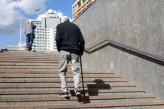 Old man with walking cane climbing stairs on city street. Concept for disability, limping adult - Powered by Adobe