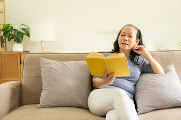 Asian senior woman reading a book on the sofa at home Activity ideas for the elderly in the family.