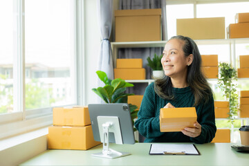 start a small business SME Asian old woman using laptop to receive and check online purchase orders to prepare product boxes Online shopping concept, parcel delivery.