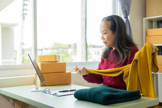 start a small business SME Asian old woman using laptop to receive and check online purchase orders to prepare product boxes Online shopping concept, parcel delivery.