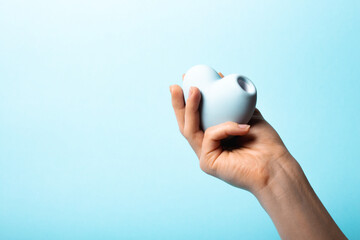 Female hand is holding blue vacuum clitoral stimulator in the shape of a heart on a blue background. Place for text. Sex shop concept. Copy space