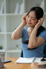 Asian woman wearing headphones sitting and working Listen to relaxing music and chat with friends on social media on laptop while sitting on weekends home office desk.