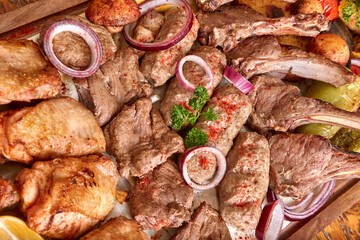 Part of the wooden board with fried meat and vegetables on the wooden table, close-up, shallow depth of field. Beef and lamb meat and kebebs in focus