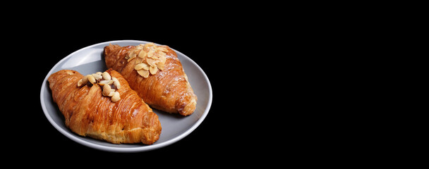 Fresh almond croissant on a plate, black background. Isolated. Space for text, banner