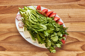 White plate with greens, tomatoes, curd cheese and radishes on the wooden table. Top view, flat lay