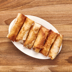 White plate with fried pita rolls with meat on the wooden table. Top view, flat lay