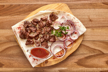 Fried beef meat with red onion rings, sauce and pita bread on the wooden board on the wooden table, flat lay top view