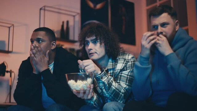 Three multiethnic friends watching horror movie, feeling frightened, guys night