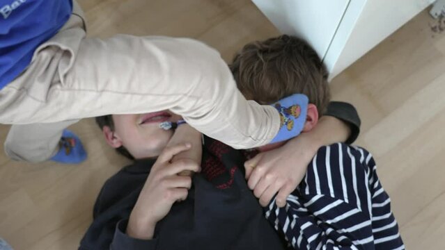 Brothers fighting each other laid on floor, wrestling. Siblings quarreling, family rivalry