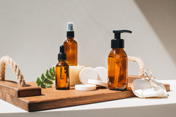 Amber bottles with facial cosmetics, liquid on a wooden tray on the light concrete background. Front view