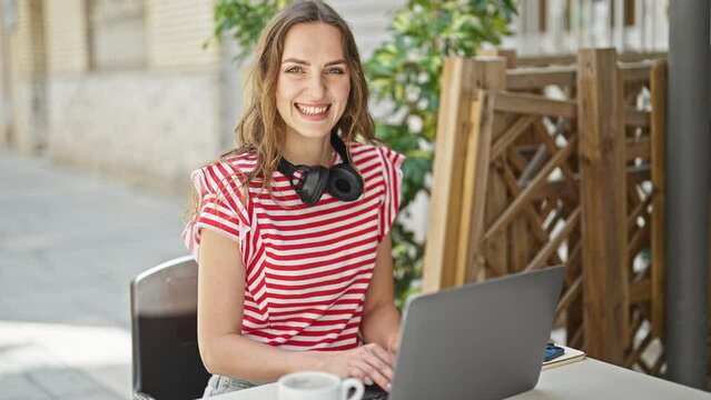 Young blonde woman using laptop sitting on table at coffee shop terrace