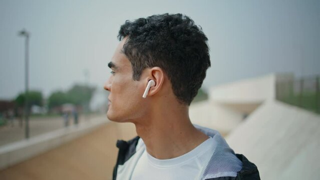 Sporty guy listening music in earphones closeup. Confident fit athlete training