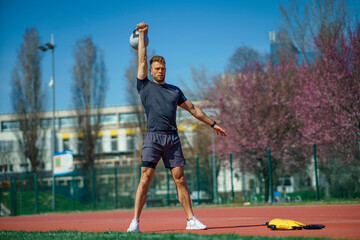 Fototapeta na wymiar Young muscular man doing exercises with kettlebell outdoor. Weightlifting workout. Sports, fitness concept.