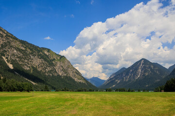 Field path between green mowed meadows towards Heiterwanger lake with mountains in the background...