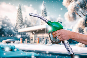 A man holds a gas station gun in his hands against the backdrop of a gas station. Fuel filling station in snowy winter.