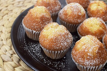 On a brown plate muffins sprinkled with powdered sugar.