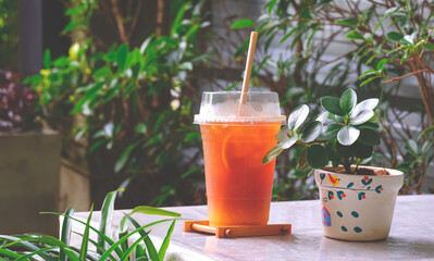 Iced fruit orange tea in plastic glass on white desk with green plant in terrace of vintage coffee shop