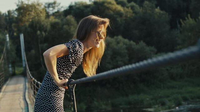 A beautiful young slender girl spits from a suspension bridge.