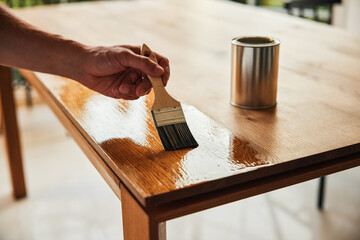 Closeup of man oiling wooden oak table with a brush