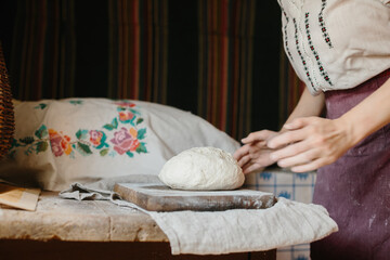 A woman in national Ukrainian embroidery kneads dough for bread.