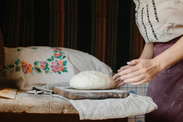 A woman in national Ukrainian embroidery kneads dough for bread.