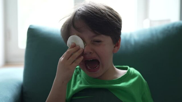 Crying small boy with hurt eye emergency, open mouth tearful child feeling pain after accident, hand covering eye with cotton